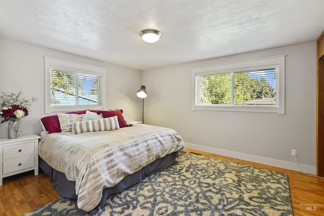 bedroom featuring baseboards, multiple windows, a textured ceiling, and wood finished floors