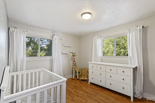 bedroom featuring a crib, light wood-style floors, and baseboards