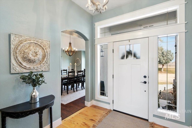 foyer with baseboards, arched walkways, light wood-style floors, high vaulted ceiling, and a notable chandelier