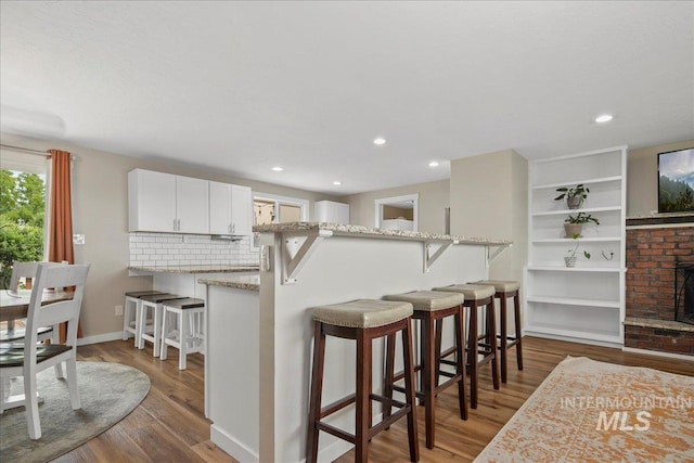 3600 S Robinson Blvd, Nampa, ID 83686 - kitchen with wood finished floors, a breakfast bar area, white cabinets, light stone counters, and backsplash