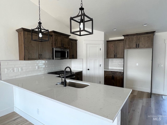 kitchen featuring kitchen peninsula, light stone countertops, sink, and hanging light fixtures