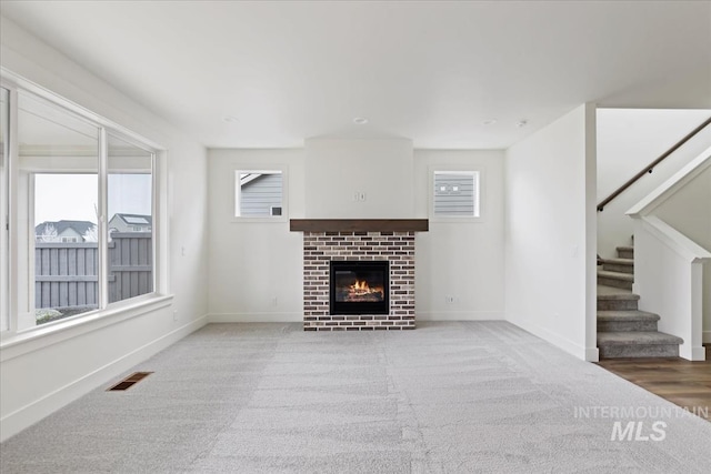 unfurnished living room featuring a brick fireplace, light colored carpet, and a healthy amount of sunlight