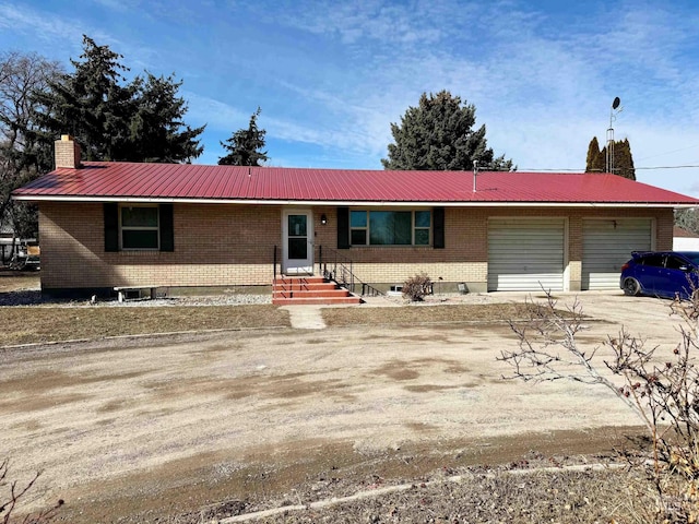 single story home featuring a garage, dirt driveway, a chimney, metal roof, and brick siding