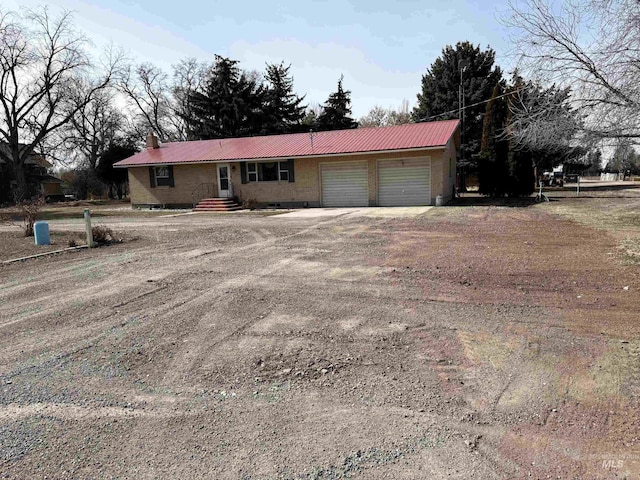 ranch-style home with an attached garage, metal roof, a chimney, and dirt driveway