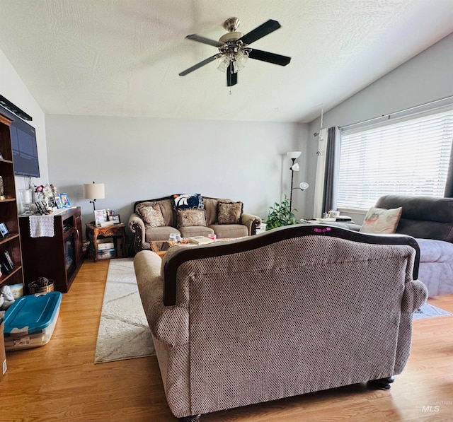 living room with lofted ceiling, ceiling fan, light hardwood / wood-style floors, and a textured ceiling