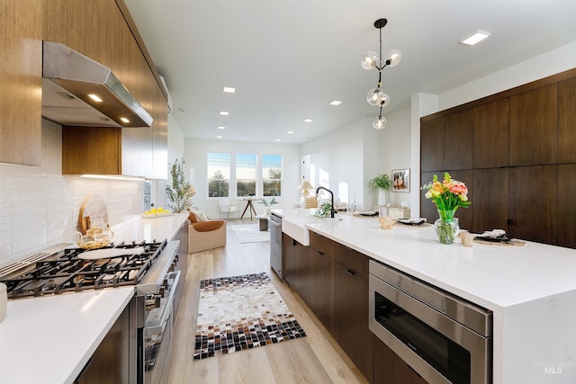 55 E State St Unit 303, Eagle, ID 83616 - kitchen with decorative light fixtures, exhaust hood, sink, light hardwood / wood-style flooring, and stainless steel appliances
