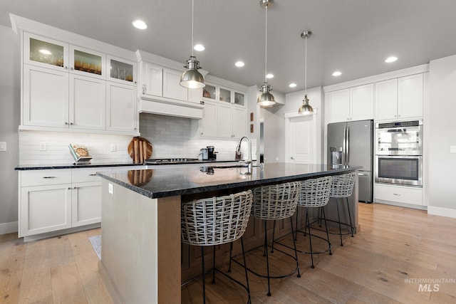 1315 N Luge Ave, Eagle, ID 83616 - kitchen featuring stainless steel appliances, light wood finished floors, a kitchen island with sink, a sink, and tasteful backsplash