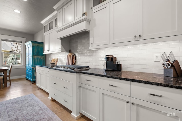 1315 N Luge Ave, Eagle, ID 83616 - kitchen with stainless steel gas stovetop, light wood finished floors, baseboards, dark stone counters, and glass insert cabinets
