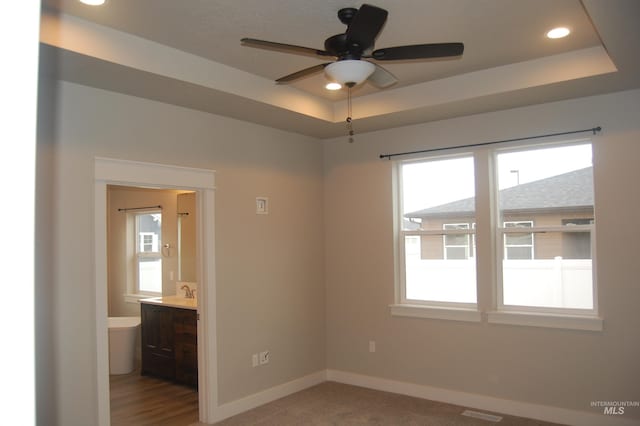 empty room with sink, ceiling fan, a tray ceiling, and plenty of natural light