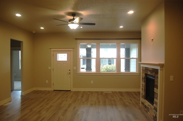 unfurnished living room with a textured ceiling, a stone fireplace, hardwood / wood-style flooring, and ceiling fan