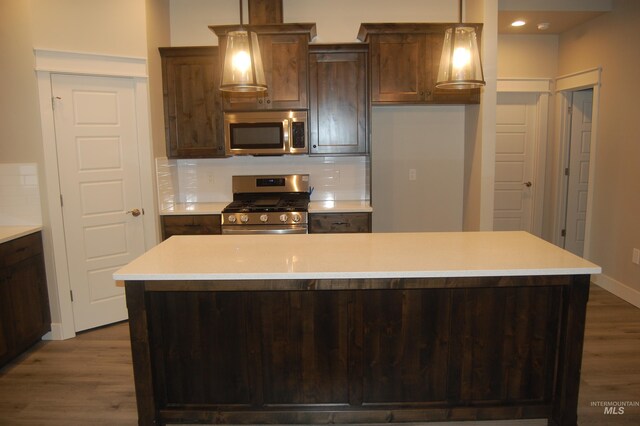 kitchen featuring decorative backsplash, hardwood / wood-style flooring, hanging light fixtures, stainless steel appliances, and a center island