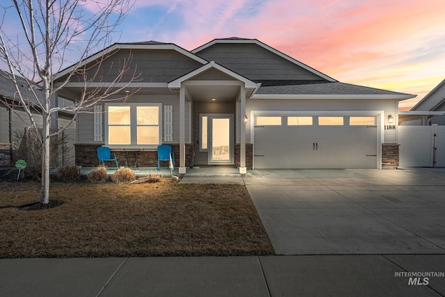 craftsman-style home with an attached garage, covered porch, fence, driveway, and stone siding