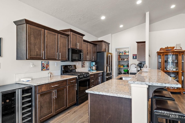 kitchen featuring lofted ceiling, wine cooler, dark brown cabinetry, a sink, and black appliances