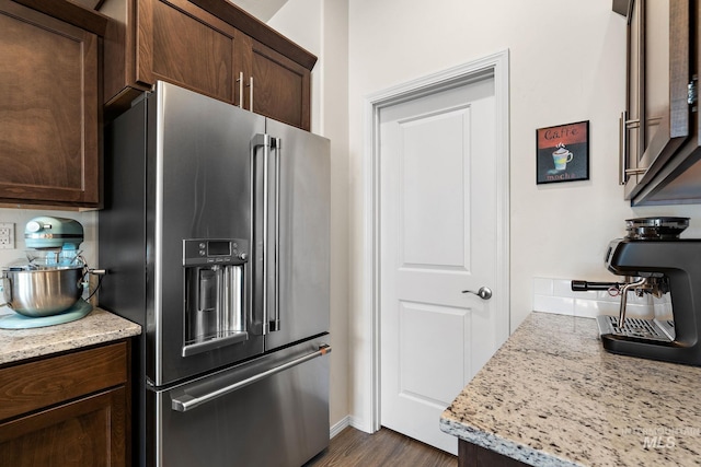 kitchen with light stone countertops, high quality fridge, dark wood-type flooring, and dark brown cabinets