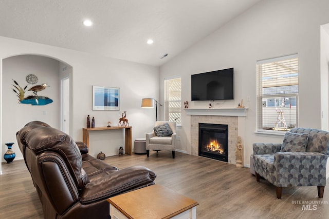 living area with a brick fireplace, plenty of natural light, vaulted ceiling, and wood finished floors