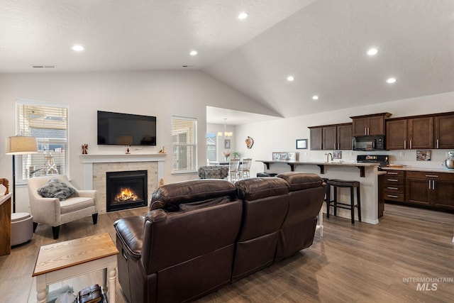 living area with visible vents, dark wood finished floors, a tiled fireplace, vaulted ceiling, and a chandelier