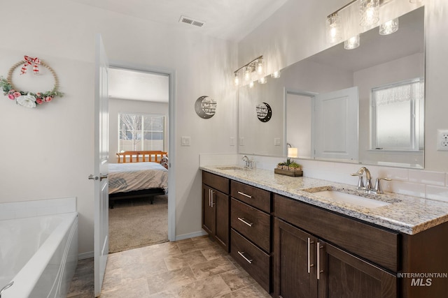 ensuite bathroom featuring double vanity, a tub, visible vents, and a sink