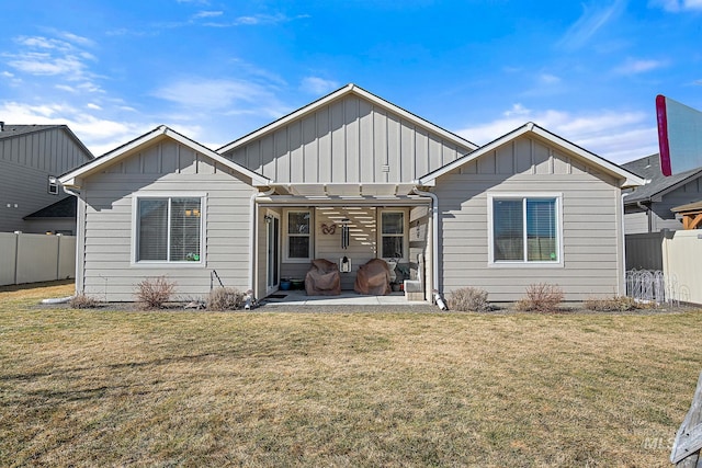 rear view of house with board and batten siding, fence, a patio, and a lawn