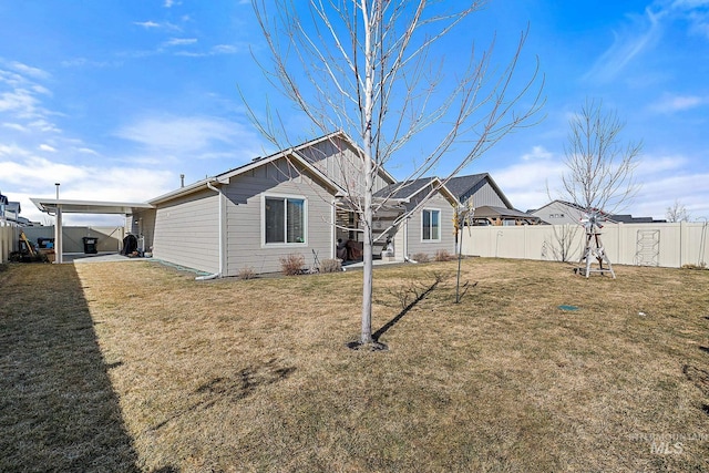 rear view of property with board and batten siding, fence, and a lawn