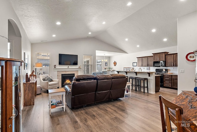 living room featuring a tile fireplace, dark wood-style flooring, a textured ceiling, high vaulted ceiling, and recessed lighting