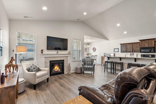 living area featuring light wood finished floors, visible vents, a glass covered fireplace, an inviting chandelier, and vaulted ceiling