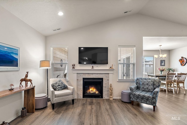 living area featuring visible vents, a glass covered fireplace, wood finished floors, vaulted ceiling, and a chandelier