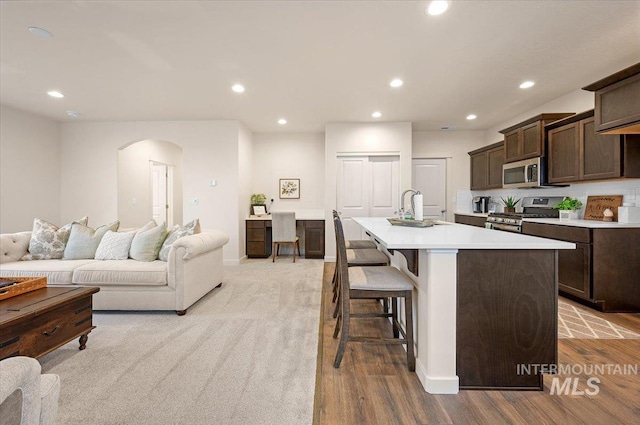 kitchen featuring sink, a breakfast bar area, appliances with stainless steel finishes, dark brown cabinetry, and an island with sink