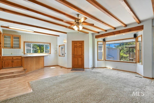 unfurnished living room featuring beamed ceiling, baseboards, ceiling fan, light wood-style floors, and a sink