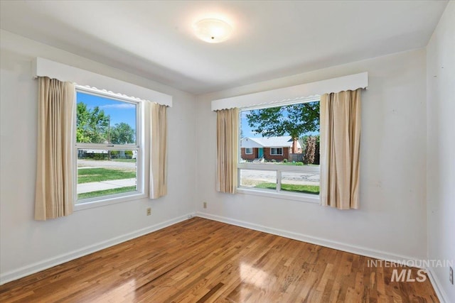spare room featuring plenty of natural light, wood finished floors, and baseboards