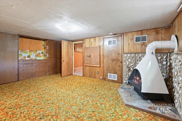 finished below grade area featuring carpet, a wood stove, wood walls, and a textured ceiling