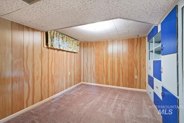 finished below grade area featuring carpet flooring, wooden walls, and a drop ceiling
