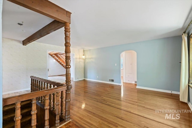 unfurnished room with arched walkways, wood finished floors, baseboards, beamed ceiling, and stairway