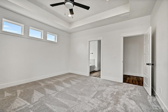 unfurnished bedroom with a raised ceiling, baseboards, carpet floors, and connected bathroom