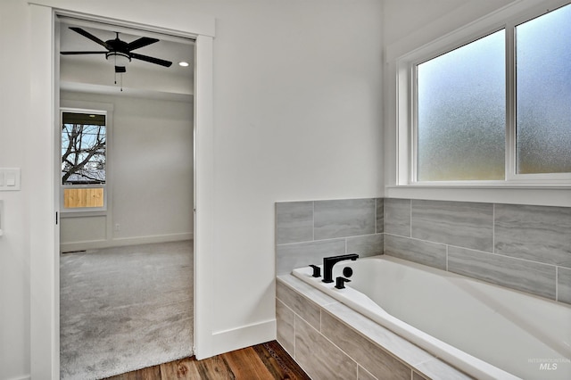 bathroom with a ceiling fan, a garden tub, wood finished floors, and baseboards