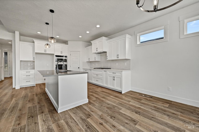 kitchen with white cabinets, appliances with stainless steel finishes, wood finished floors, and a sink