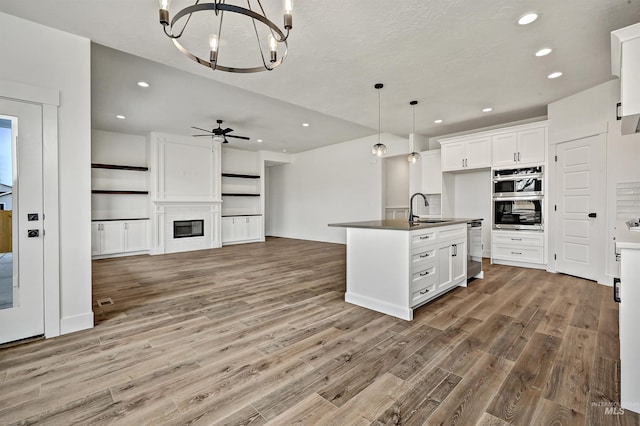 kitchen featuring dark countertops, open floor plan, wood finished floors, stainless steel double oven, and a sink