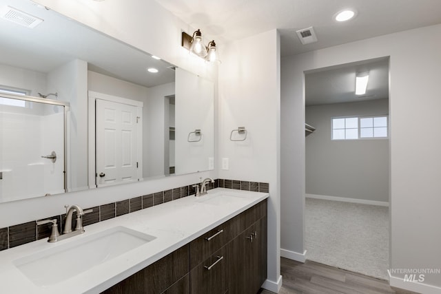 bathroom with a sink, a shower with door, and visible vents