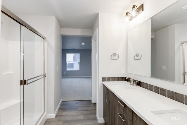 bathroom with double vanity, wood finished floors, a stall shower, and a sink