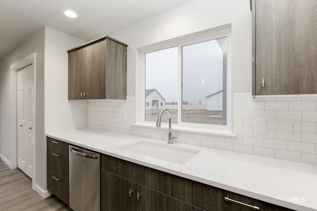 kitchen with stainless steel dishwasher, light wood-style flooring, tasteful backsplash, and a sink