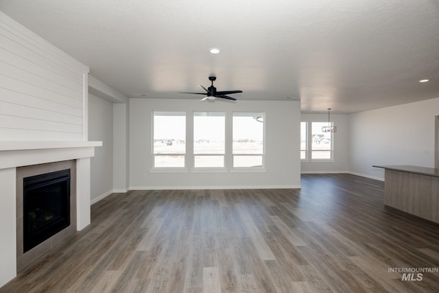 unfurnished living room featuring dark wood finished floors, ceiling fan with notable chandelier, a fireplace, and baseboards