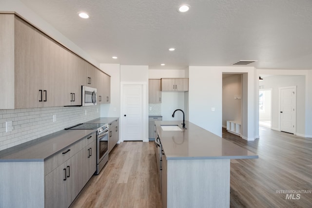 kitchen featuring light wood-type flooring, visible vents, a center island with sink, a sink, and stainless steel appliances