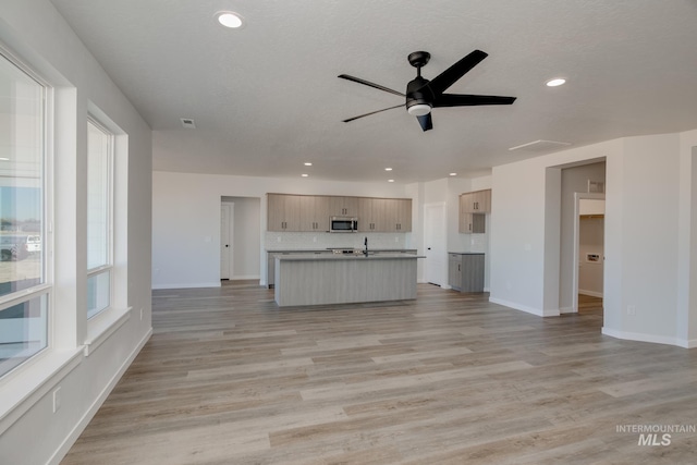 kitchen featuring light wood-type flooring, recessed lighting, open floor plan, stainless steel microwave, and tasteful backsplash