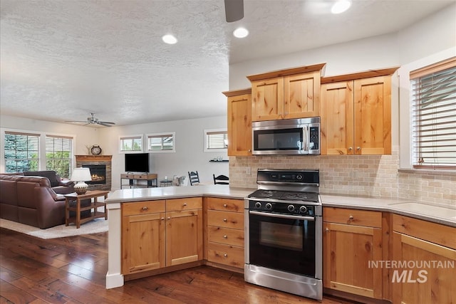 2479 N Devlin Ave, Meridian, ID 83646 - kitchen with stainless steel appliances, a ceiling fan, a textured ceiling, a peninsula, and a warm lit fireplace