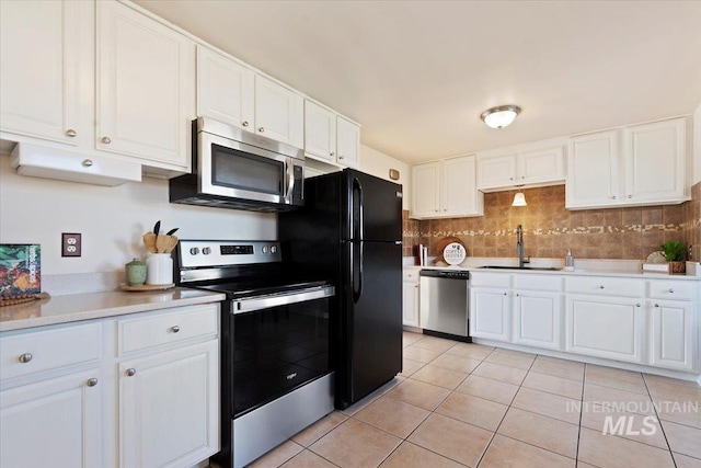 kitchen with sink, decorative backsplash, light tile patterned floors, appliances with stainless steel finishes, and white cabinetry