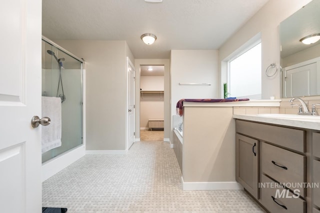full bathroom with a shower stall, vanity, a walk in closet, baseboards, and a bathtub