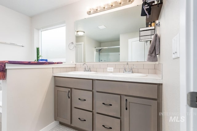 bathroom with a stall shower, a sink, double vanity, and tasteful backsplash