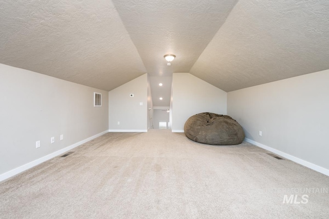 additional living space with baseboards, vaulted ceiling, visible vents, and a textured ceiling