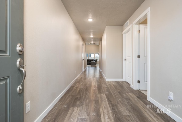 hallway featuring dark wood finished floors, baseboards, a textured ceiling, and visible vents