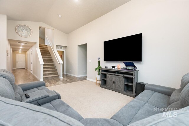 carpeted living area featuring stairway, baseboards, visible vents, and high vaulted ceiling