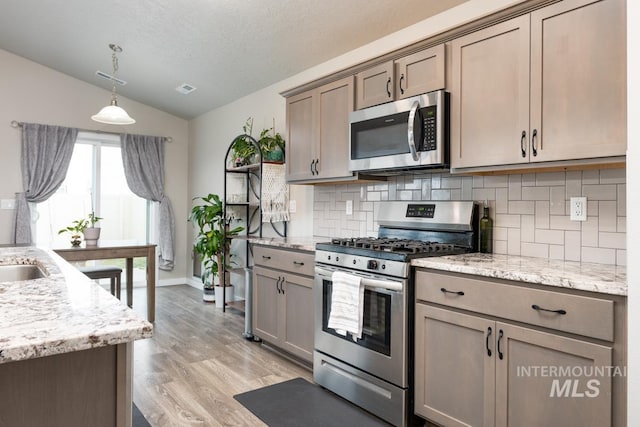 kitchen with vaulted ceiling, tasteful backsplash, light wood-style floors, pendant lighting, and appliances with stainless steel finishes